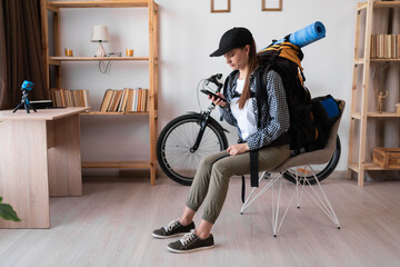 Female hiker with backpack ready to travel sitting in the living room reading travel information...