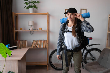 Smiling young female traveler hiker ready to trip with backpack making a small size gesture at...