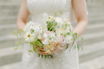 Beautiful bridal bouquet held by a bride wearing a sparkling dress during an outdoor wedding ceremony