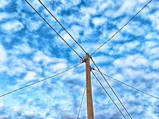 Power lines stretch across the sky under a beautiful cloud-filled blue canopy during the evening
