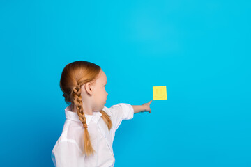 Young girl in uniform pointing at a smiling sticky note on a blue background, showcasing cheerful...