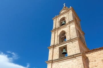 Fototapeta premium Serene Bell Tower Silhouette: A weathered stone bell tower stands tall against a vibrant azure sky, its bells patiently awaiting the call to chime.