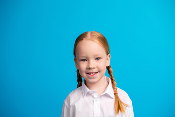 Smiling schoolgirl in white shirt with braids standing against bright blue background, embodying...