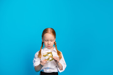 Young schoolgirl in a white shirt examining a sparkling gold geometric model against a solid bright...
