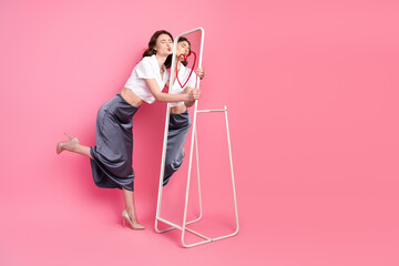 Charming Woman in Stylish Outfit Kissing a Mirror with Heart Drawing on a Pink Background