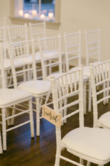 Elegant white chairs arranged for a wedding ceremony with reserved signs and soft candlelight ambiance