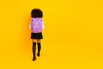 Rear view of a schoolgirl with a purple backpack on a vibrant yellow background emphasizing youth...