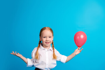 Happy young schoolgirl holding red balloon in hand against bright blue background wearing white...