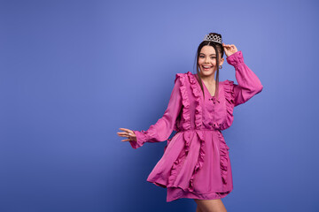Charming young woman in a vibrant pink ruffle dress wearing a crown, smiling joyfully against a...