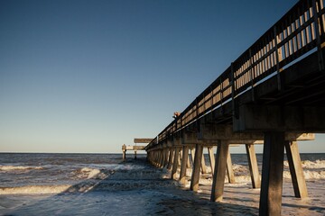 Obraz premium Pier over ocean at sunset with clear blue sky.