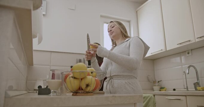 Two young women peel and chop apples in a bright modern kitchen, preparing a healthy and delicious meal together.