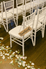 Reserved seating at a wedding ceremony with decorative petals on a wooden floor seen during the afternoon light