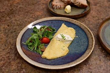 A freshly served omelette with arugula and cherry tomato salad on a rustic ceramic plate