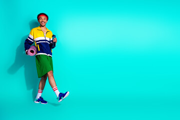 Young man in vintage activewear holding fitness gear and water bottle against vibrant turquoise...