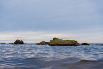 Rocky coastline under an overcast sky. Large boulders in calm water along the shore create a...