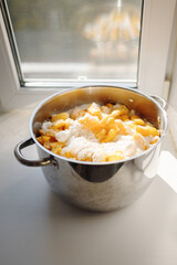 Close-up of sliced apricots with sugar in a metal pot placed by the window. Ingredients for making...
