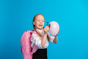 Young girl in school attire holding a balloon and laughing, set against a bright blue background,...
