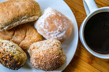 Fototapeta premium Selection Or Group Of Baked Mixed Mini Bread Rolls With A Mug Of Black Coffee Beverage