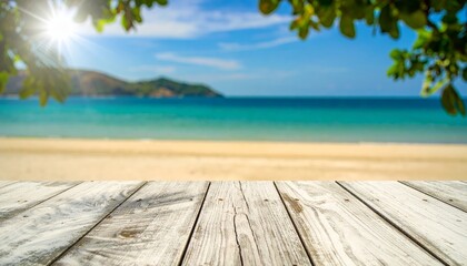 Fototapeta premium Sunny beach scene with clear blue sky, calm turquoise sea, sandy shore, and blurred green leaves framing the wooden deck foreground.