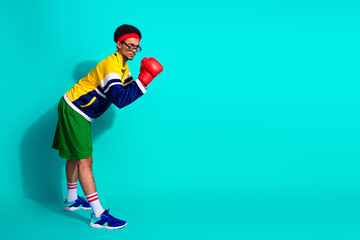 Funny sporty man in retro attire with boxing gloves poses confidently against bright turquoise...