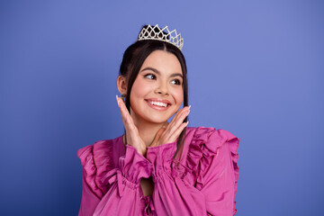 Elegant young woman wearing a tiara and vibrant pink dress posing on a purple background,...