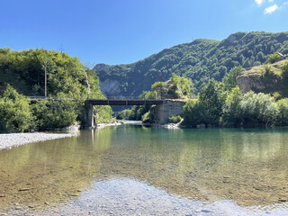 A calm river with clear water, a small bridge over the river and lush green hills