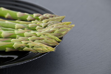 Fresh asparagus spears arranged on a black plate, ready for a healthy meal.
