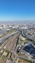 Imagem aérea da movimentada Avenida Radial Leste cortando a Zona Leste de São Paulo, com fluxo intenso de veículos, bairros ao redor e estrutura urbana