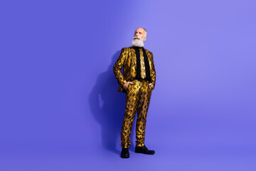 Senior man in glamorous gold suit posing confidently against a vibrant purple backdrop, embodying...