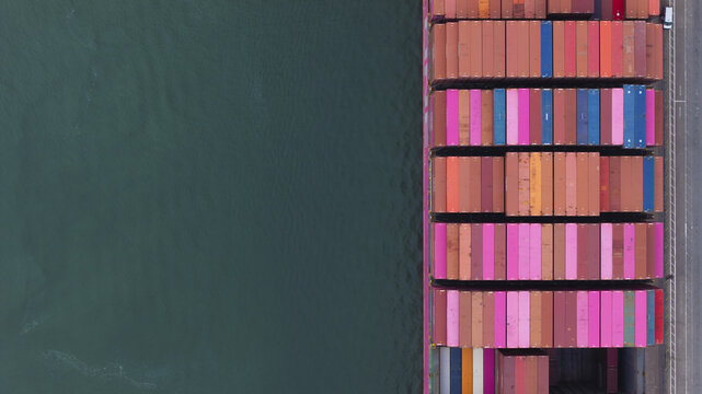 Long Beach, United States - 07 April 2025: Aerial view of a container ship docked at the Port of Oakland, its stacked cargo a vibrant mosaic against the deep teal waters.