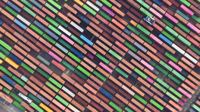Long Beach, United States - 07 April 2025: Aerial view of a geometric tapestry of stacked shipping containers, their varied hues creating a vibrant mosaic against the stark industrial landscape.