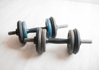 Two vintage dumbbells with worn rubber grips and colorful weight plates resting on a light wooden floor, showcasing fitness equipment for strength training and exercise routines