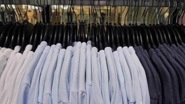 Row of white cotton t shirts on black hangers in clothing store. Close up view. Fashion retail and casual apparel concept