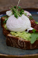 Delicious open-faced sandwich served on rustic bread with mashed avocado, crispy bacon, perfectly poached eggs and a topping of fresh microgreens.