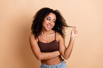 Charming young woman with curly hair posing confidently against a beige backdrop in a casual and...