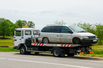 Tow Truck Transporting a Damaged Minivan on a Country Roadside with 24-Hour Assistance Service