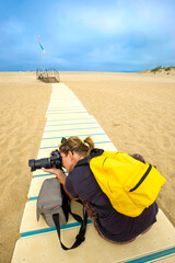 young woman with a yellow bacpack photographing Dune desert of Piscinas at Ingurtosu, Sardinia, Italy
