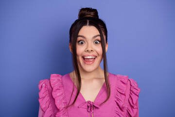 Cheerful young woman in pink ruffled dress posing in front of a purple background with a surprised...