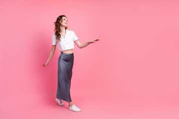 Attractive young woman wearing elegant summer outfit posing against pink background in a casual and...