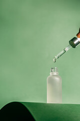 A frosted dropper bottle of facial serum stands against a green background, perfect for use in...