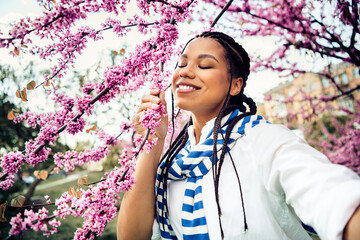Cute woman enjoying springtime surrounded by vibrant blooming flowers in an urban park under bright...