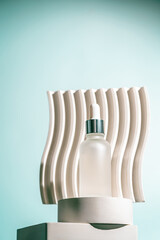 A frosted dropper bottle of facial serum is placed on a sculpted white pedestal with a soft teal...