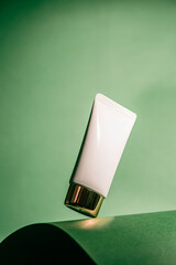 A white tube of soothing face cream against a green background, ideal for use in skincare ads,...