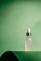 A frosted dropper bottle of facial serum stands against a green background, perfect for use in...