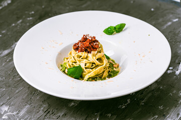 Fitucini pasta with balognese sauce and pesto in a white plate with wide sides on a gray background. High quality photo
