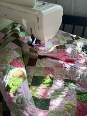 Pink and Green Patchwork Quilt on Sewing Machine During Stitching. Modern Hobby Concept. Handheld...