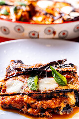 Eggplants alla parmesano on a white plate on a wooden table with a white napkin. Baked eggplants...