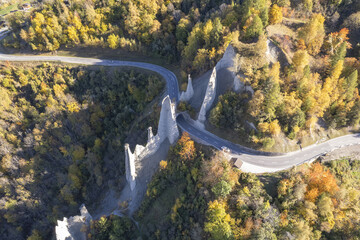 Aerial view of winding roads carving through the earth pillars, autumnal trees ablaze in golden hues, a symphony of nature's artistry, HÃ©rÃ©mence, Valais, Switzerland.