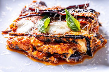 Eggplants alla parmesano on a white plate on a wooden table with a white napkin. Baked eggplants with tomatoes and cheese according to a traditional Italian recipe. Close-up. High quality photo