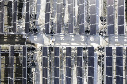 Aerial view of solar panels glinting under the sun, a grid of modern energy poised against the muted tones of the ground below, location data omitted.